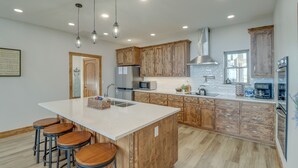 Cocina moderna con gabinetes de madera, una isla grande con taburetes, electrodomésticos de acero inoxidable e iluminación colgante.