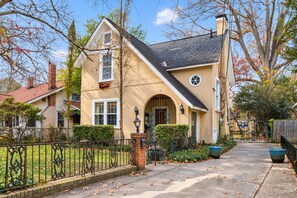 A two-story house with a front entrance, a visible chimney, and a small front yard with a metal fence.
