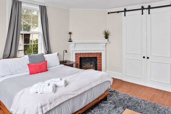 A bedroom with a bed, a fireplace, a wardrobe, and a window with curtains. - Simplicity on Sims | 3BR 1BA | Downtown (Columbia)