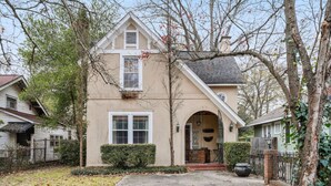 A two-story house with a beige exterior, a front entrance with a small porch, and a visible window. - Simplicity on Sims | 3BR 1BA | Downtown (Columbia)
