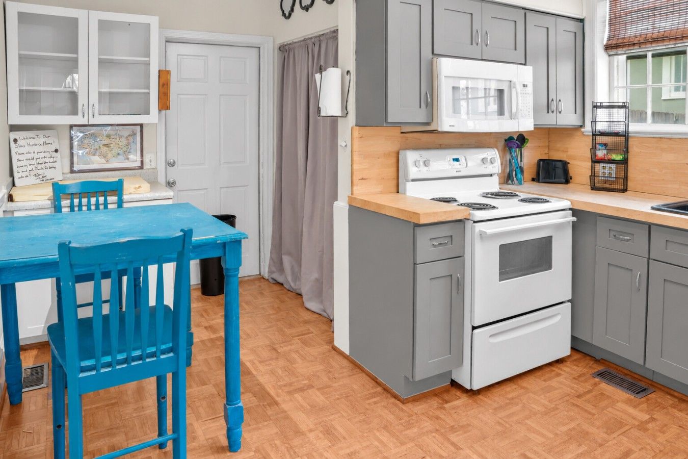 A kitchen with grey cabinets, a white stove, and a blue table with chairs.