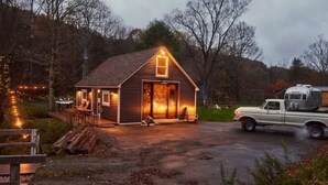 Eine kleine Holzhütte mit Veranda, ein Lkw davor und eine Lichterkette am Wegesrand.