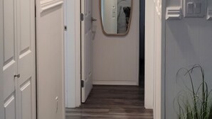 A hallway with white doors, a wooden floor, a mirror on the wall, and a potted plant. - Otter House
Close to the Beach (Tulameen)