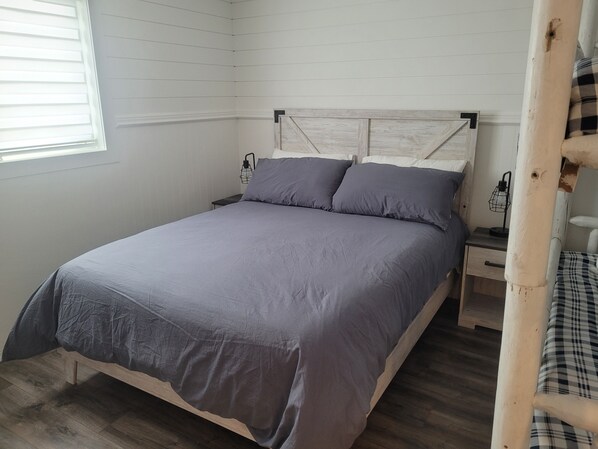 Un dormitorio con cabecera de madera, colcha gris y mesita de noche con lámpara.