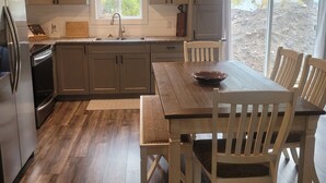 A modern kitchen with wooden cabinets, a dining table with chairs, a refrigerator, and a window with blinds. - Otter House
Close to the Beach (Tulameen)