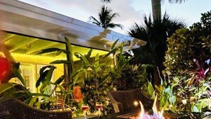 An outdoor seating area with wicker chairs, a fire feature, and lush tropical plants. - Tropical Paradise in BEST LOCATION! Walk to everything! Heated pool! (Cape Coral)