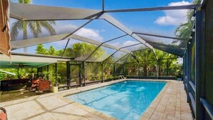 A covered swimming pool with a clear view of the surrounding greenery and a patio area with seating. - Tropical Paradise in BEST LOCATION! Walk to everything! Heated pool! (Cape Coral)