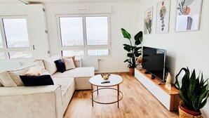 A modern living room with a sofa, a coffee table, a TV, and artwork on the wall. - Charming Apartment With Panoramic Seine River & Eiffel Tower Views (Ivry-sur-Seine)