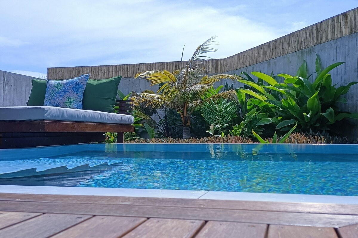 A pool area with a wooden deck, a sofa with cushions, and various plants.