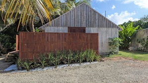 Un bâtiment en bois doté d’un toit en pente, entouré d’une clôture en bois et de plantes tropicales.