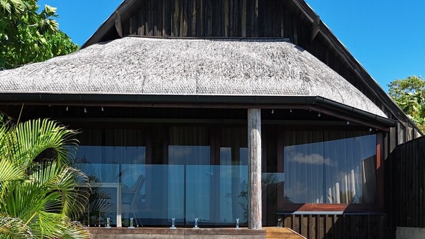 Une villa en bois dotée d’une piscine, d’un espace salon extérieur abrité et d’une végétation luxuriante.