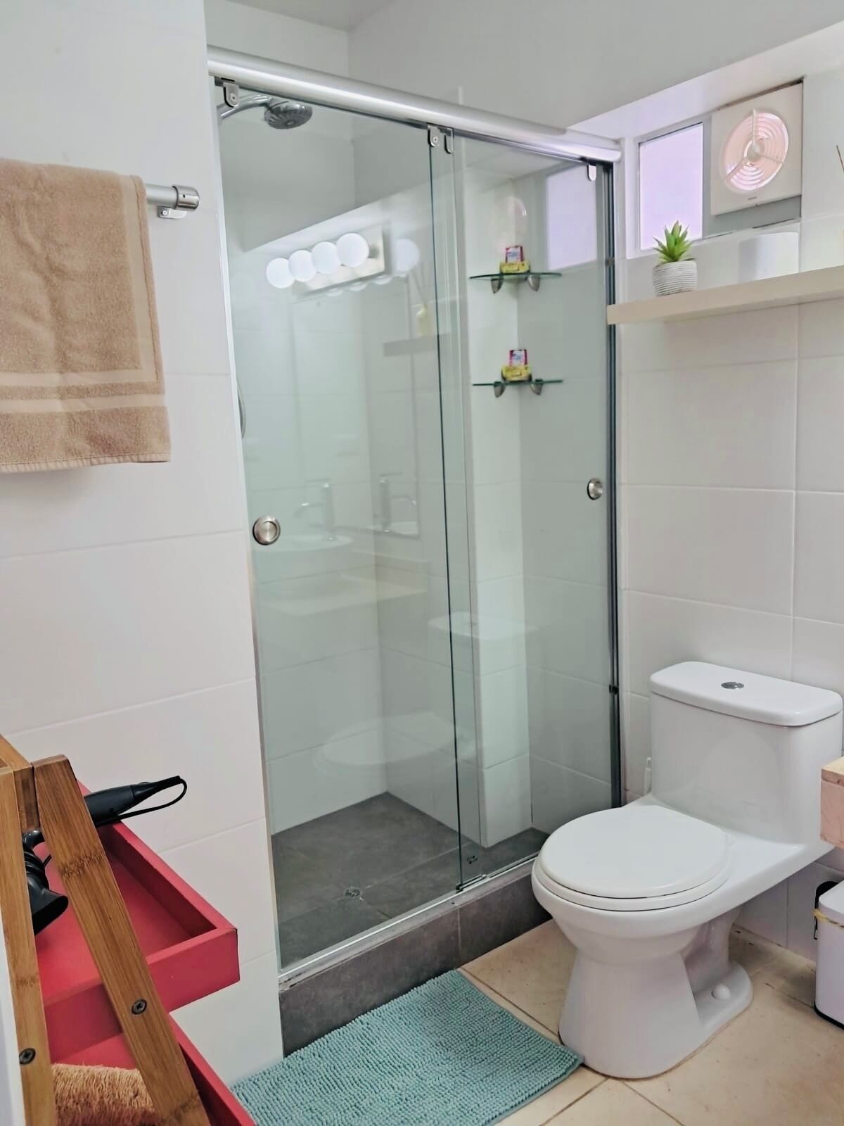Uma casa de banho moderna com cabine de duche em vidro, sanita e uma pequena prateleira com artigos de higiene pessoal.