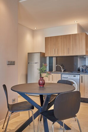 A modern kitchen with wooden cabinets, a stainless steel refrigerator, a dishwasher, and a dining area with a round table and two chairs.