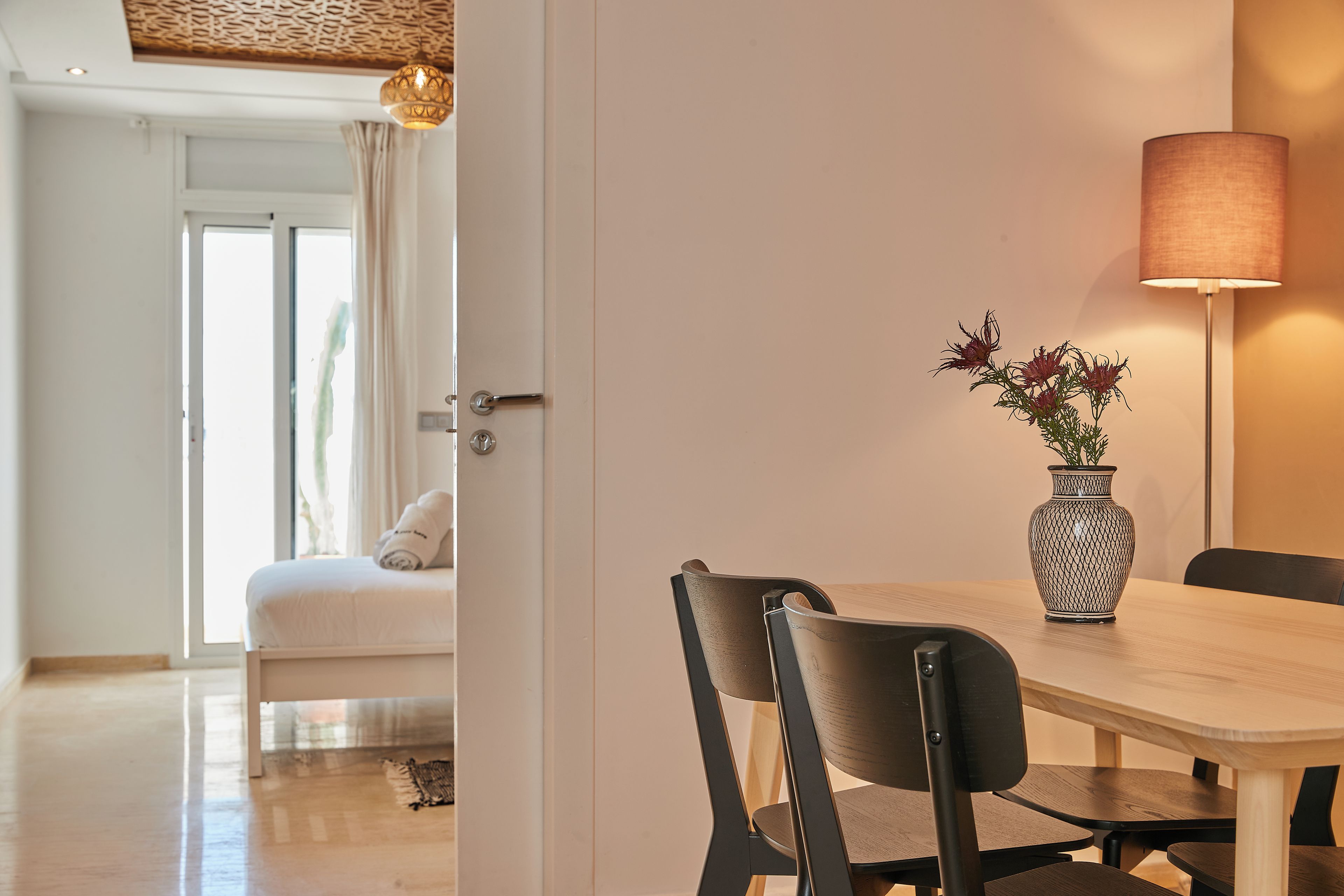 Un coin repas avec une table en bois, deux chaises, un vase de fleurs et un lampadaire.