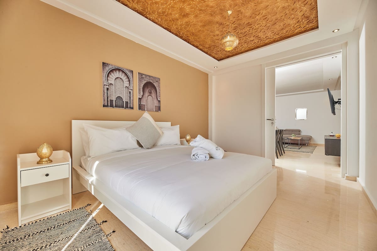 A modern bedroom with a large bed, a nightstand, and a ceiling with a textured design.