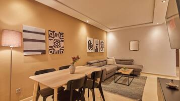 Uma sala de estar moderna com área de jantar, apresentando um sofá, uma mesa de centro e uma televisão.