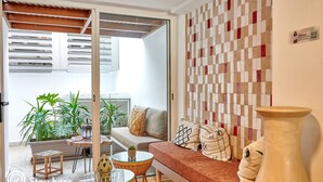 A modern living room with a sofa, a coffee table, and a large vase. There is a glass door leading to a balcony with plants. - Stayhere Rabat - Hassan Heritage (Rabat)