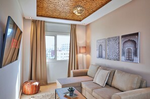 Un salon moderne avec un canapé, un pouf et un téléviseur à écran plat.
