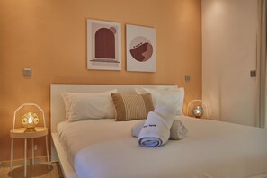 Un lit bien fait, avec des draps blancs, deux oreillers et une serviette enroulée. Deux appliques murales sont fixées de chaque côté du lit.