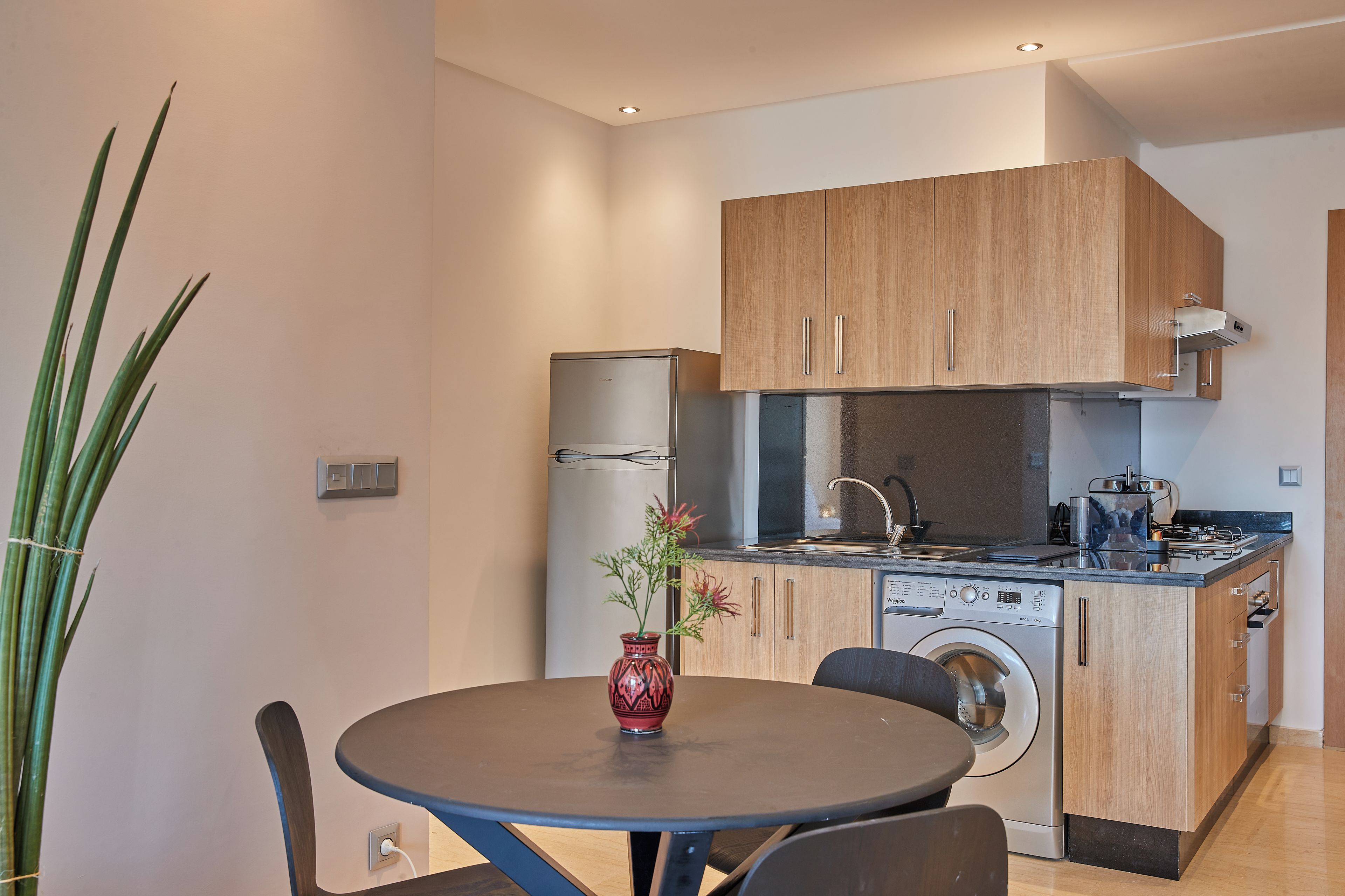 Une cuisine moderne avec des meubles en bois, un lave-linge encastré et un coin repas comprenant une table et des chaises.