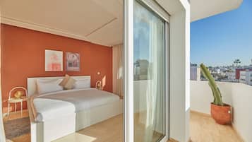 A modern bedroom with a large bed, a glass door leading to a balcony, and a city view.
