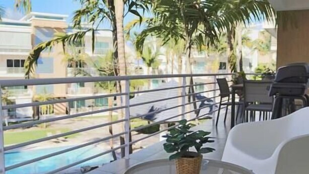 Un balcón con vista a una piscina, una silla de mimbre y una pequeña planta en maceta.