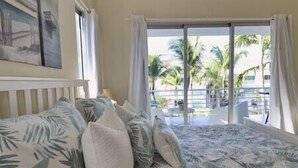 Habitación de hotel con cama, vista a palmeras y una piscina a través del ventanal.