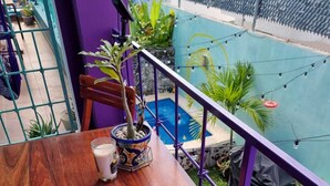 A wooden table with chairs, a potted plant, and a glass of milk on a balcony with a purple railing. - Luna - Alexa art loft w extras -  bicycles & snorkel gear. shared pool & grill (Cozumel)