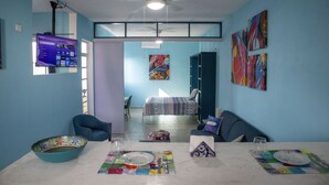 A dining area with a table set for two, a blue chair, a bowl, and a TV mounted on the wall. - Luna - Alexa art loft w extras -  bicycles & snorkel gear. shared pool & grill (Cozumel)