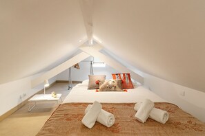 A modern, well-lit attic bedroom with a bed, pillows, a bedside table, and a lamp. - Metamorphosis - Nazaré Retreat (Nazaré)
