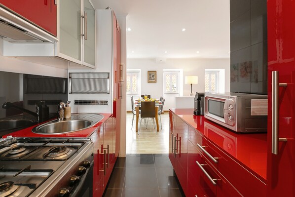 A modern kitchen with red cabinetry, stainless steel appliances, and a central island. - Metamorphosis - Nazaré Retreat (Nazaré)