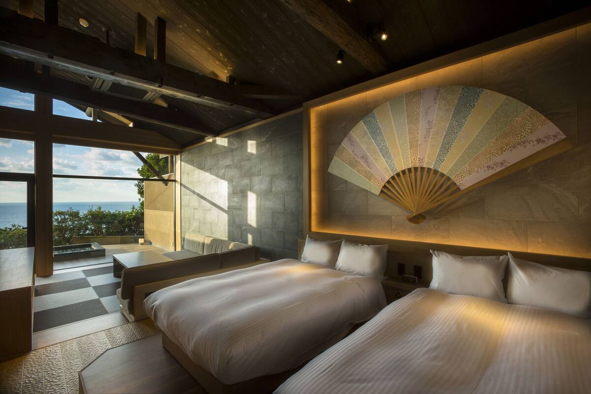 A modern hotel room with a large bed, a fan, and a view of the ocean.