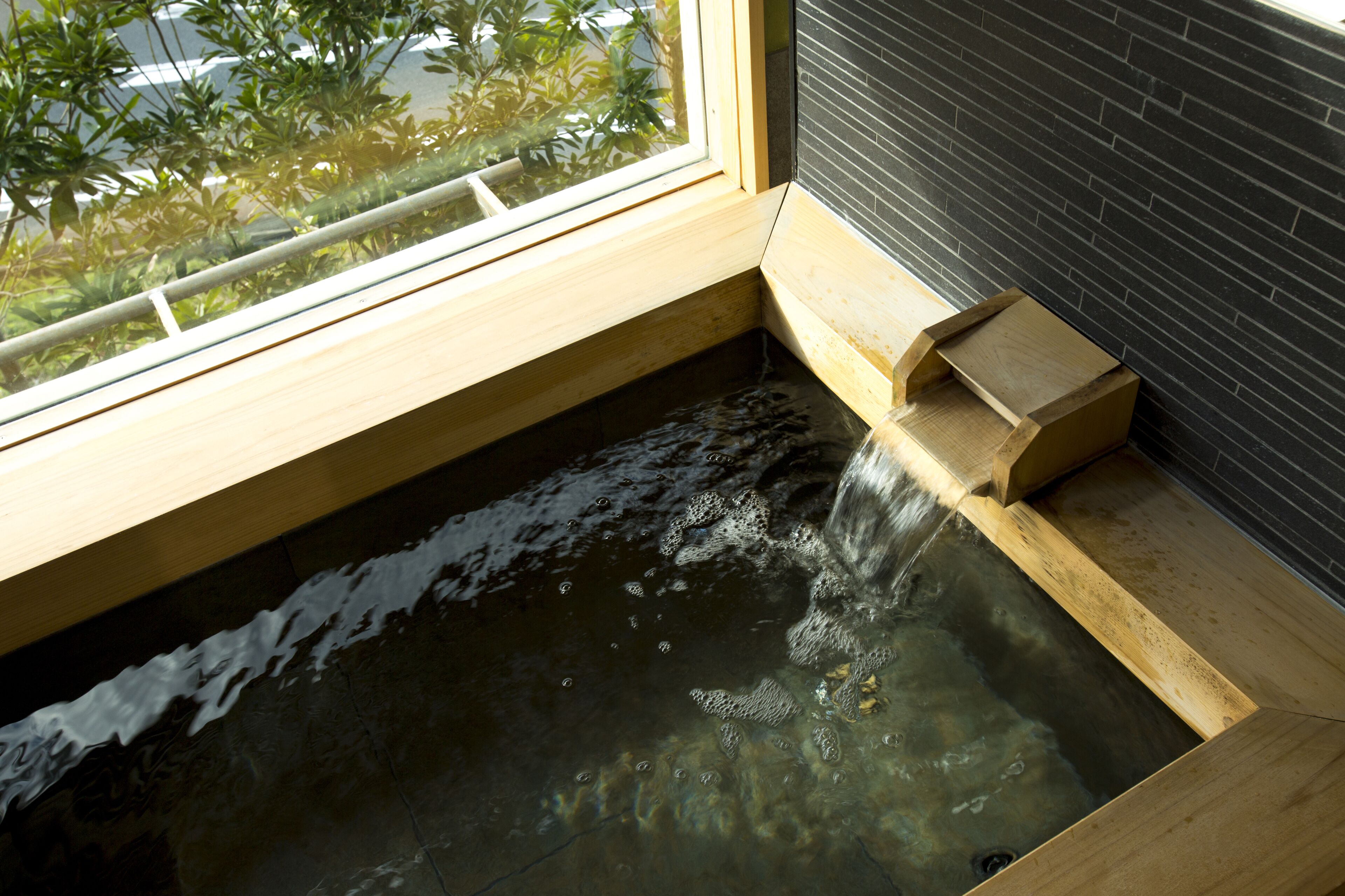 A wooden bathtub with a wooden ledge and a window above it.