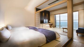 A modern hotel room with a large bed, a desk, and a view of the ocean.