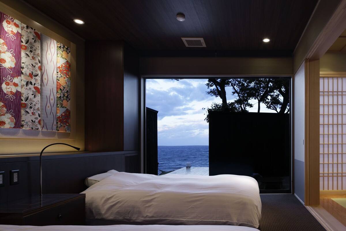 A hotel room with two beds, a large window with a view of the sea, and a traditional Japanese sliding door.