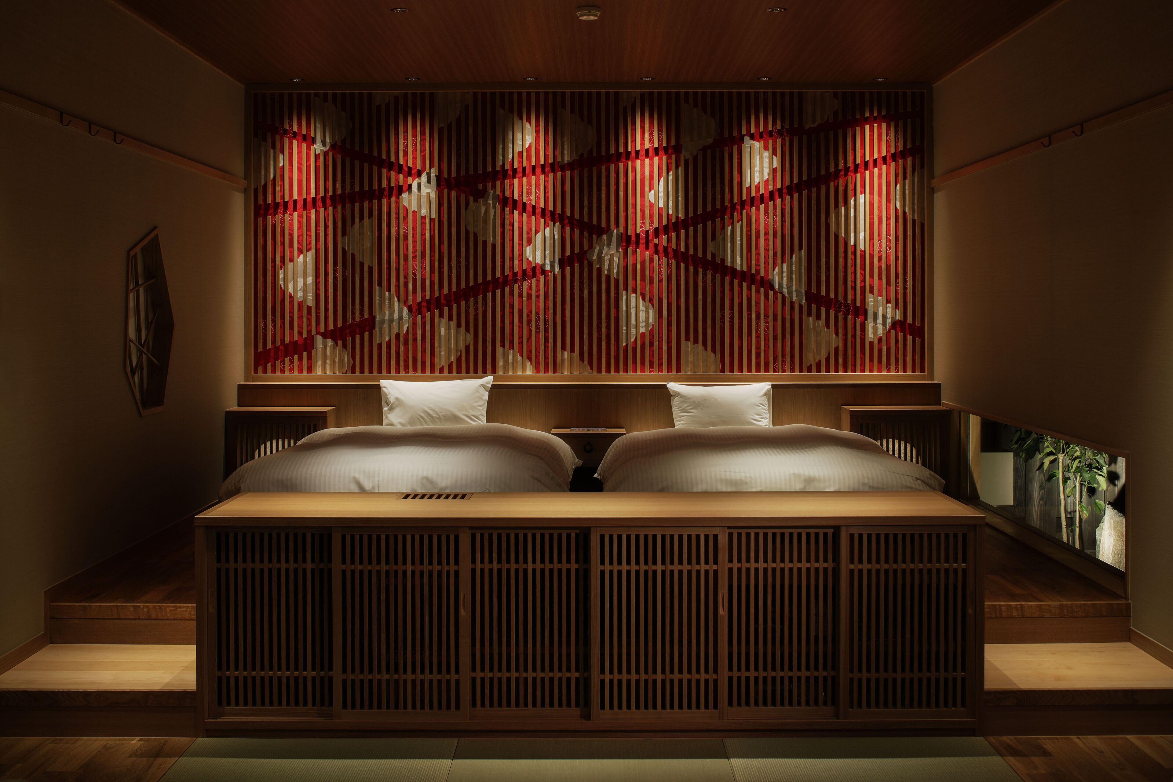 A room with a low wooden bed, a wall with vertical slats, and a small plant on the right.