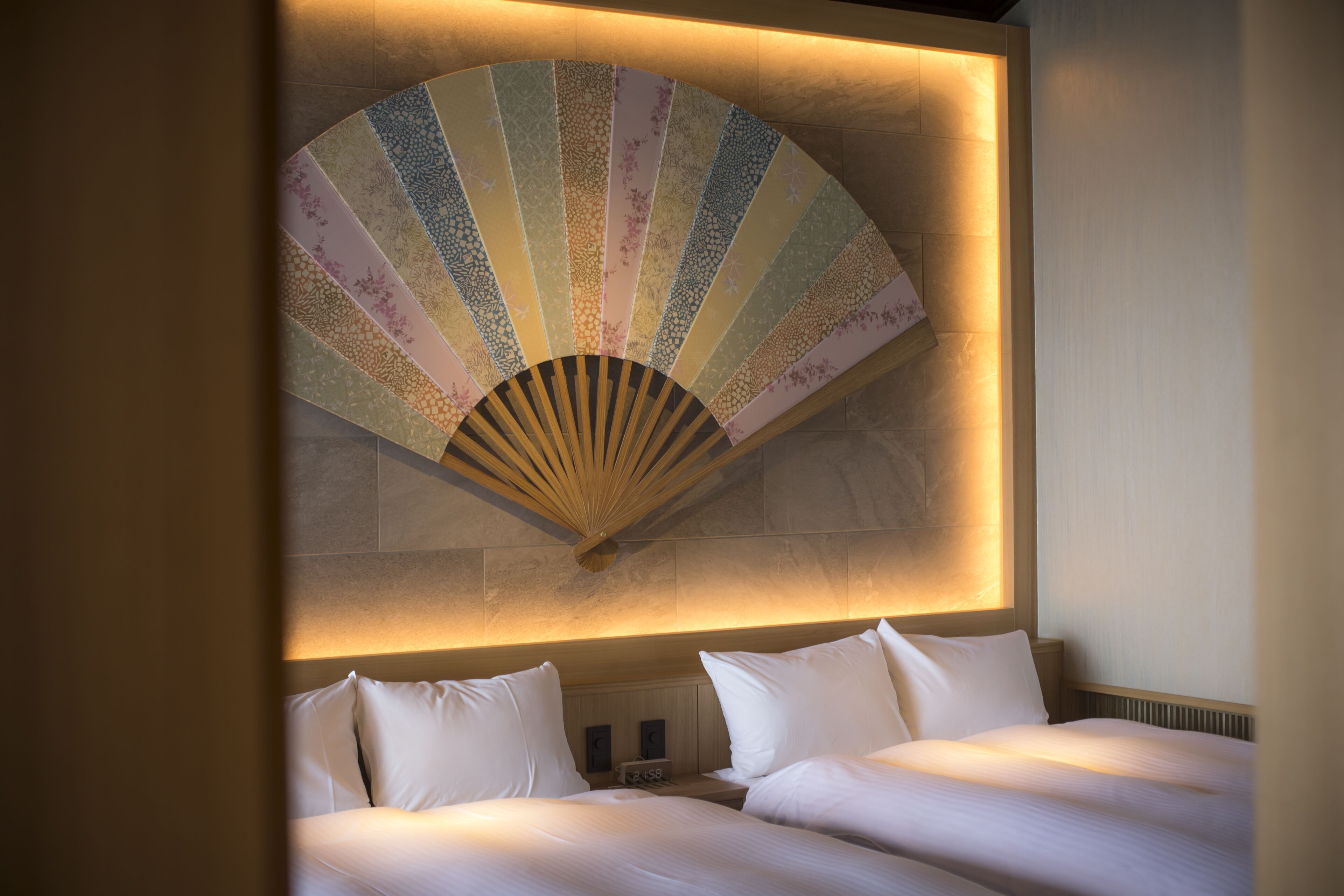 A hotel room with two beds, a large decorative fan, and a wall-mounted clock.