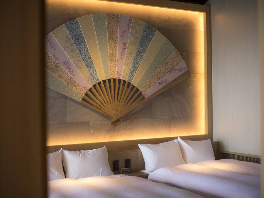A hotel room with two beds, a large decorative fan, and a wall-mounted clock.