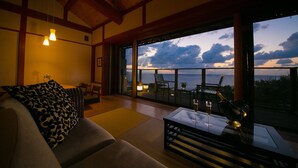 A cozy living room with a sofa, a table with a glass, and a view of the ocean at dusk.