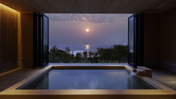 A modern spa with a large hot tub, wooden flooring, and a view of the ocean at dusk.