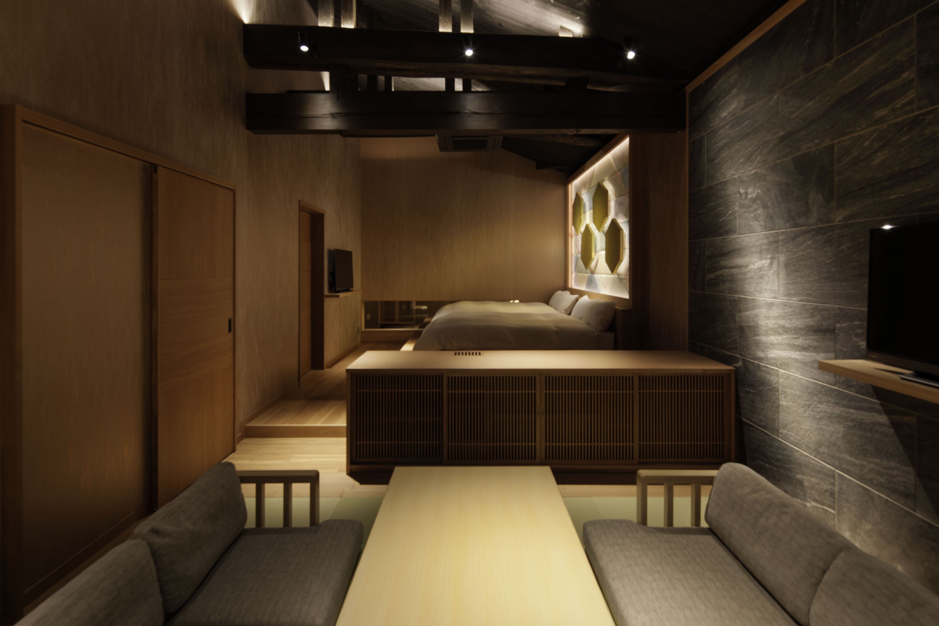 A modern hotel room with a wooden floor, a sofa, a bed, and a TV.