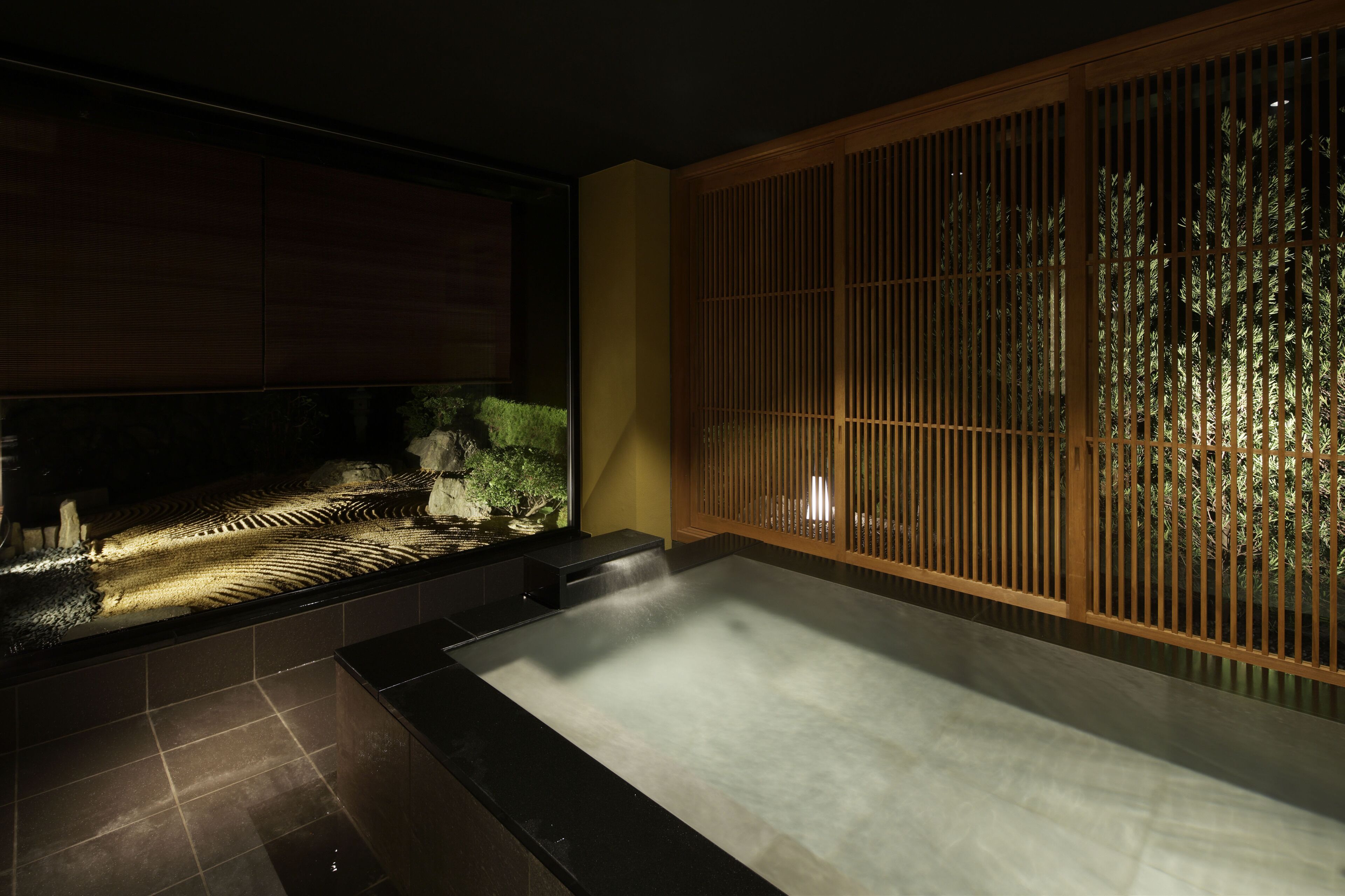 Un spa moderno con un amplio jacuzzi, un muro divisor de madera y un pequeño jardín interior.
