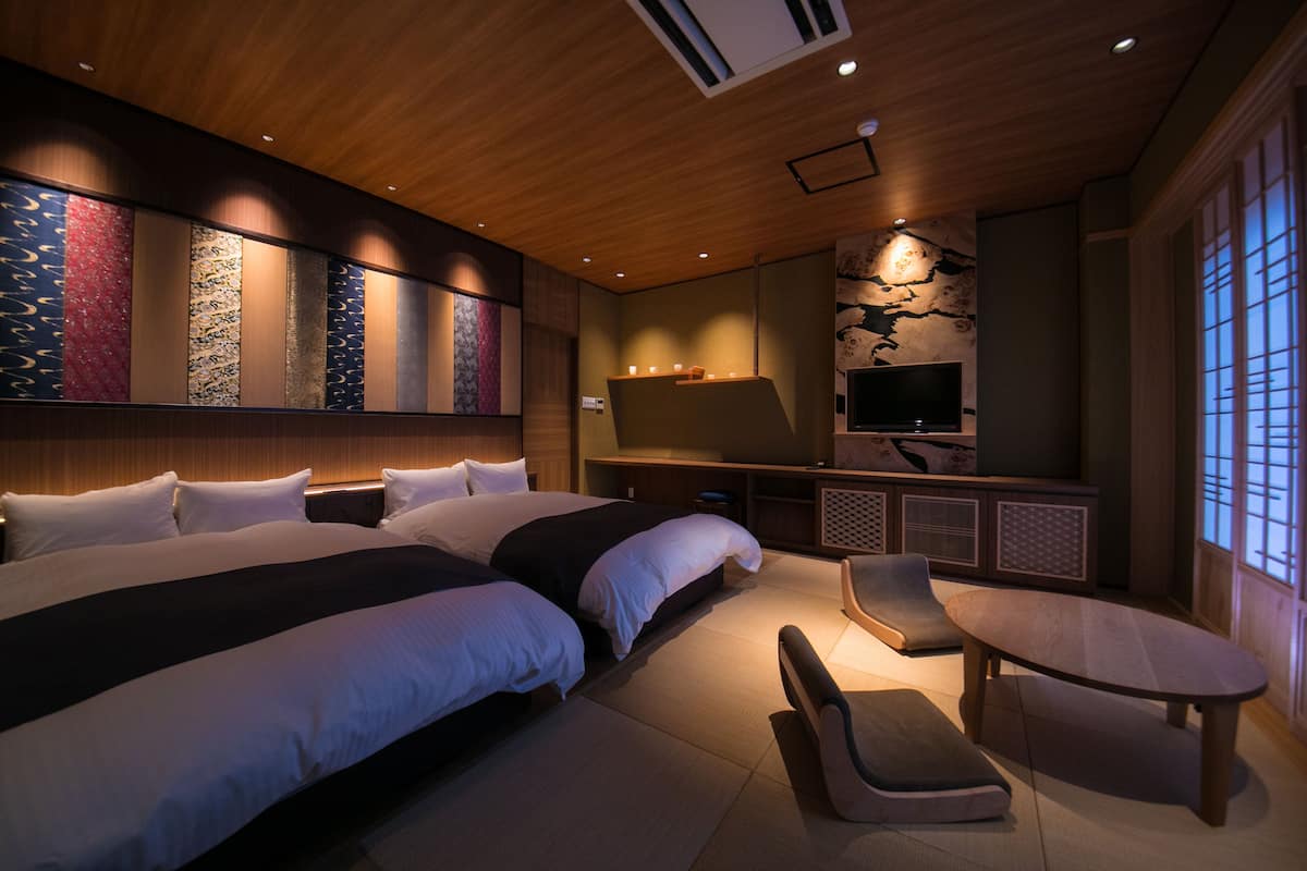 A modern hotel room with a large bed, a TV, a seating area, and a decorative wall.