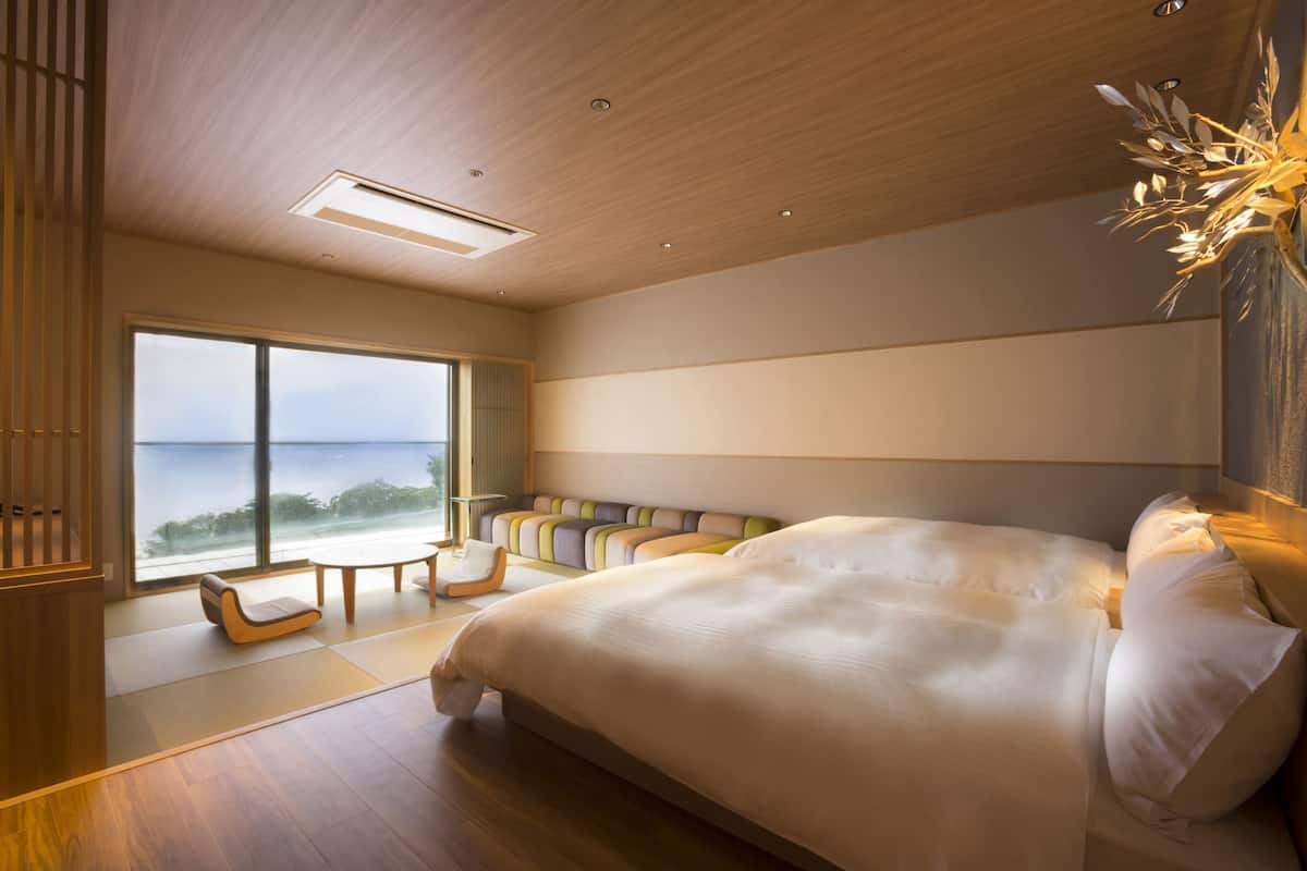 A spacious bedroom with a large bed, a view of the sea, and a seating area with a table.