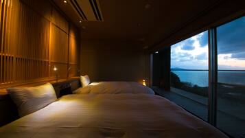 Un dormitorio moderno con una cama grande, una mesita de noche y vistas al mar a través de amplias ventanas.