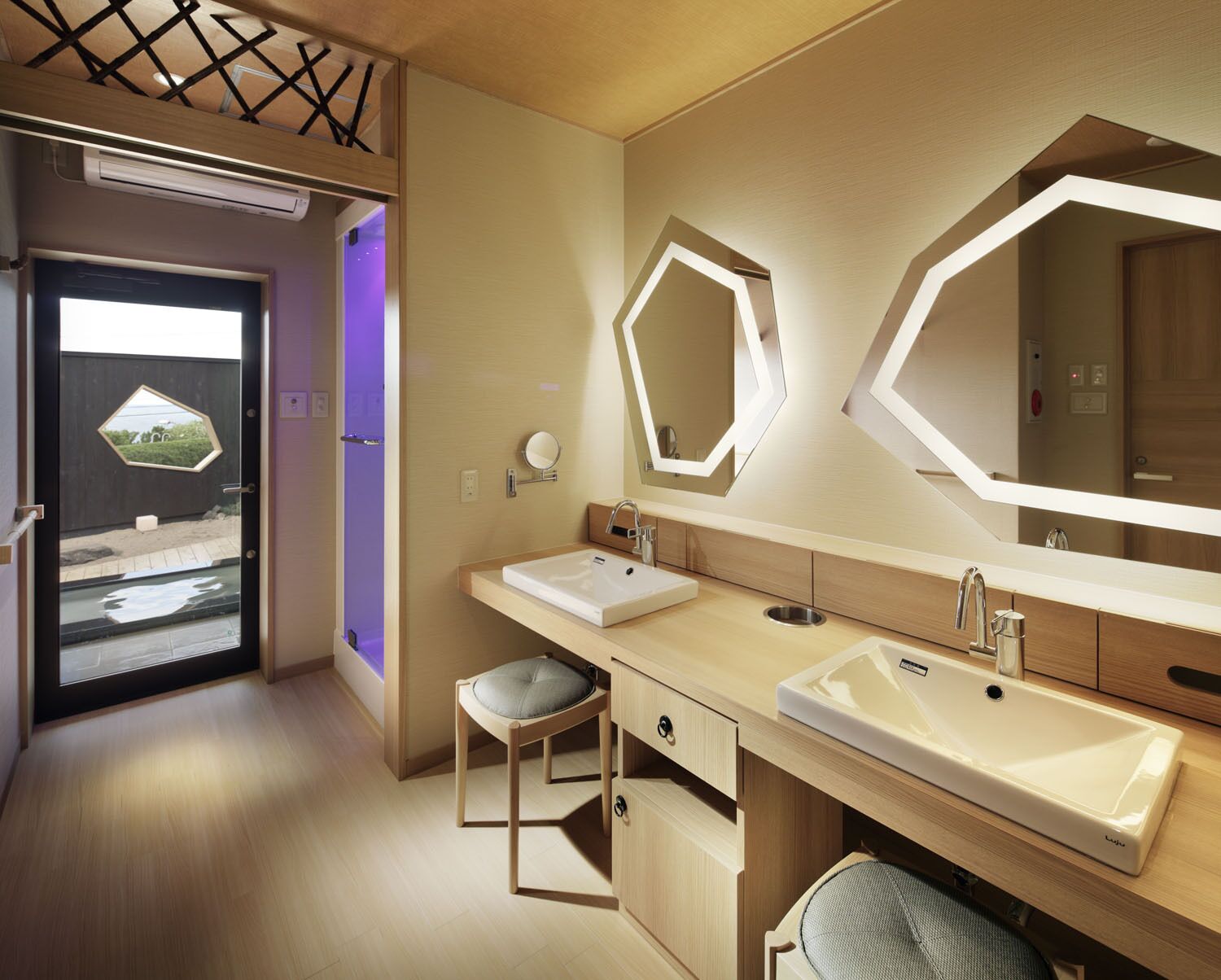 A modern bathroom with two sinks, a large mirror, and a stool.