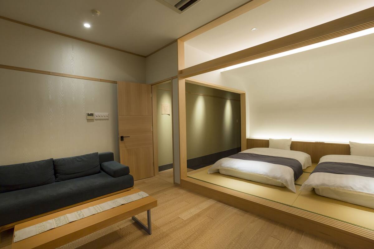 A hotel room with a sofa, two beds, a mirror, and a wooden floor.