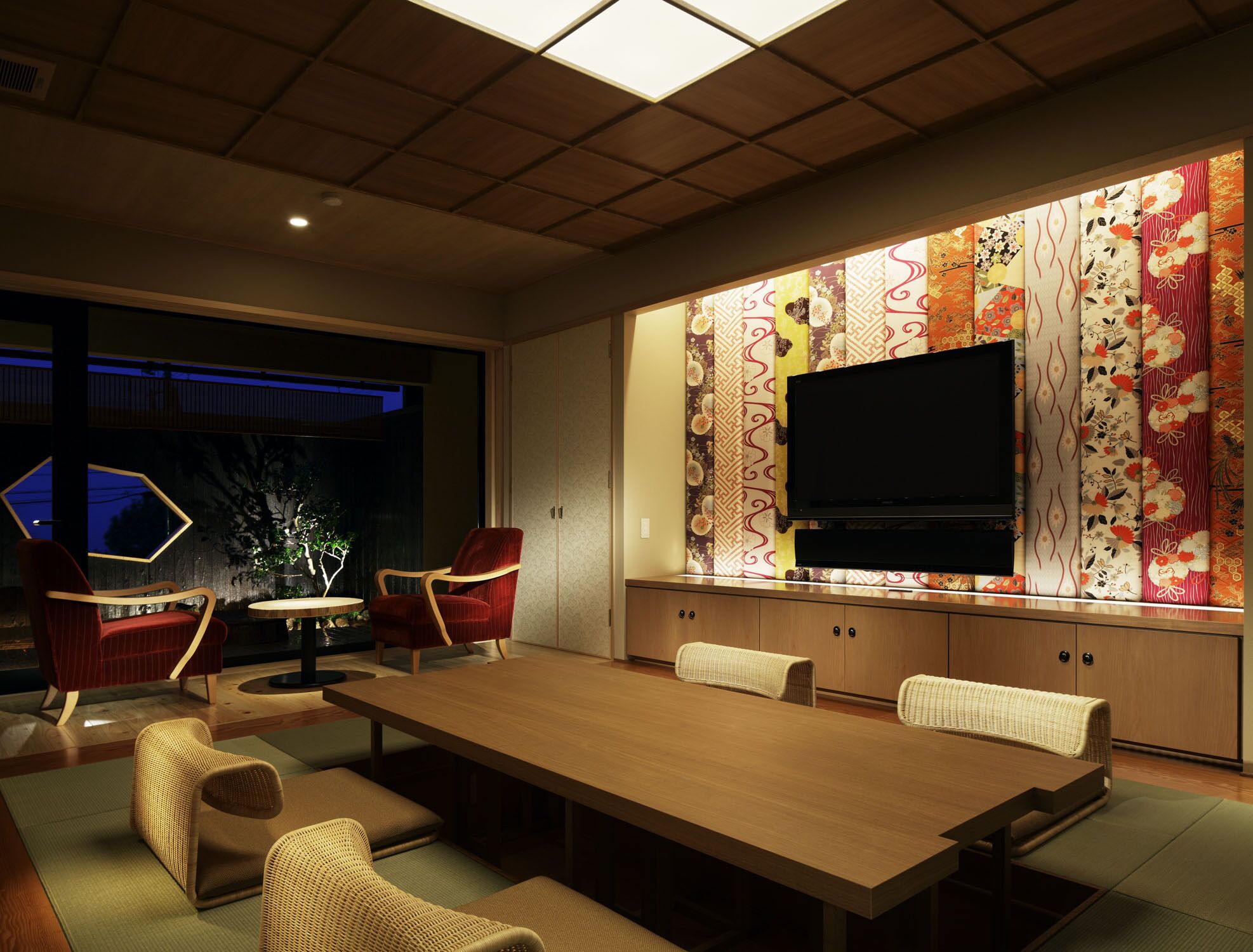 A modern living room with a large wooden table, comfortable seating, a flat-screen TV, and a decorative wall with traditional patterns.