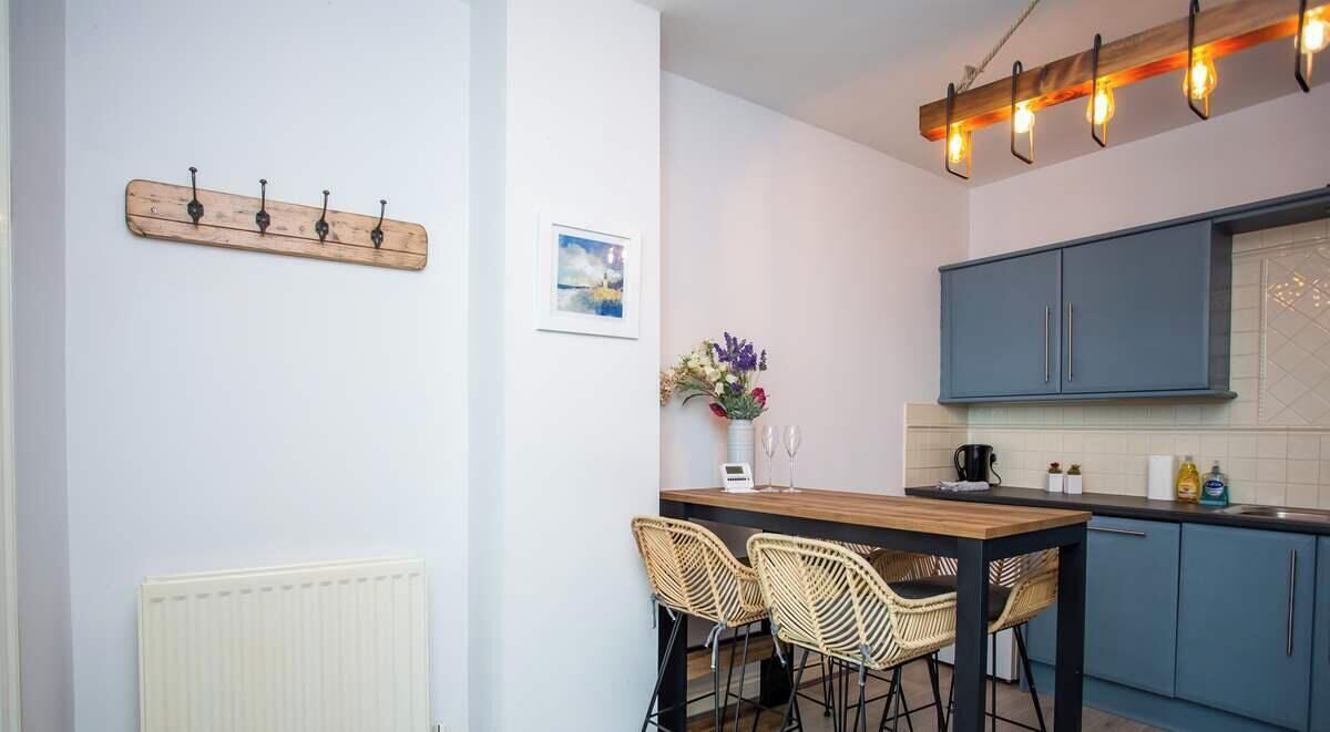 A kitchen with a wooden table, two wicker chairs, a white radiator, a blue cabinet, and a light fixture.