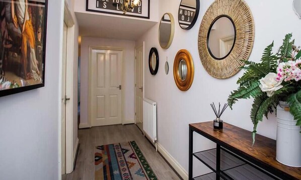 Un couloir avec une porte, un radiateur, un miroir et une petite table sur laquelle est posée une plante.
